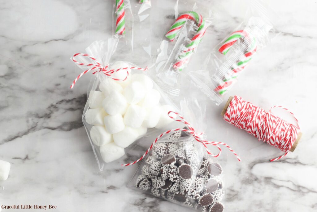 Small plastic bags filled with marshmallows and chocolate candy pieces tied with red and white twine, sitting on a marble countertop.