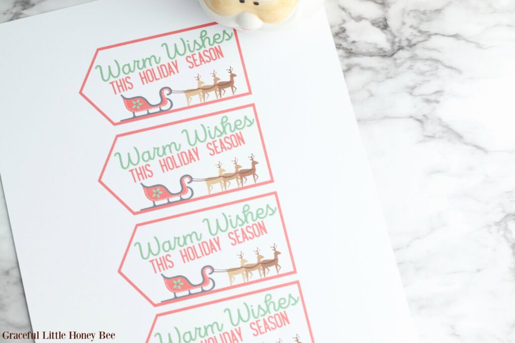 Printed gift tags for Santa Mug Gifts sitting on a marble countertop.