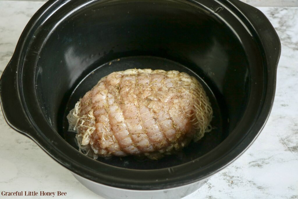 Raw boneless turkey breast roast in a black slow cooker.
