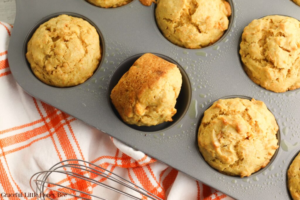 Baked muffins in a muffin tin with an orange and white plaid tea towel.