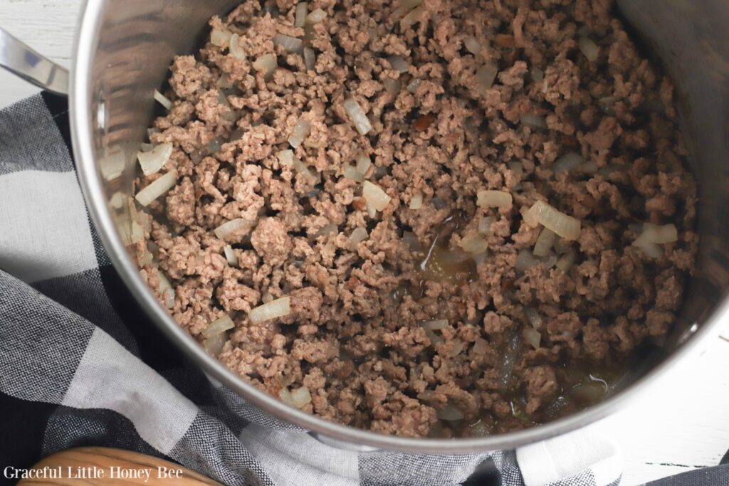 Cooked ground beef and oinion in a stainless steel pot.