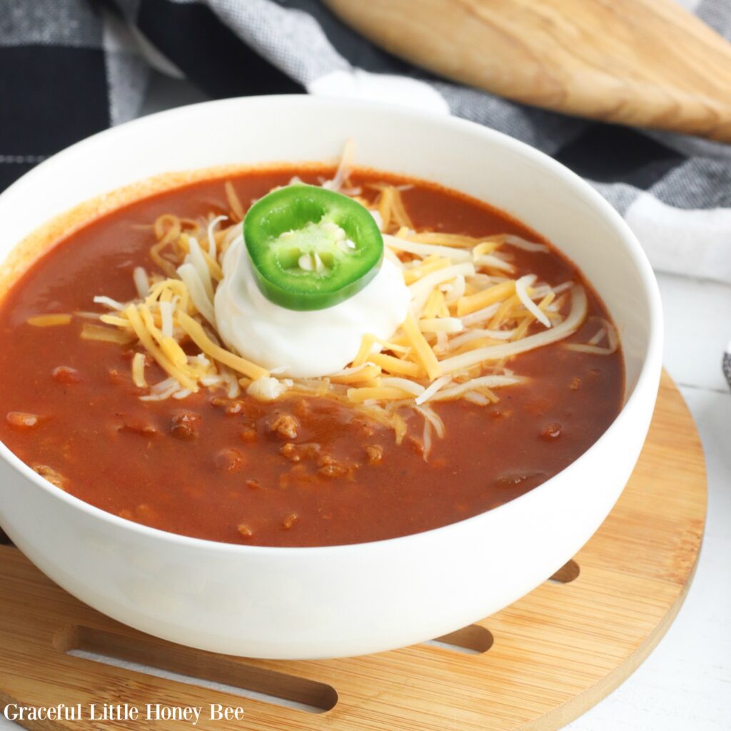 V8 Chili in a white bowl with shredded cheese, sour cream and garnished with a jalapeno.