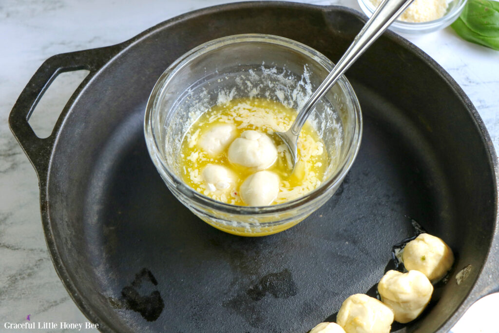 Bread dough balls dipped in butter in a small glass dish inside of a cast iron skillet.