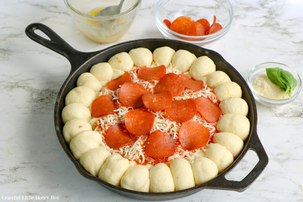 Pizza dip layered with pepperoni surrounded by raw bread dough in a cast iron skillet.