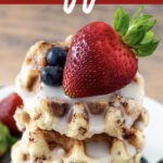 Cinnamon Roll Waffles stacked on a plate drizzled with glaze and topped with fresh fruit.