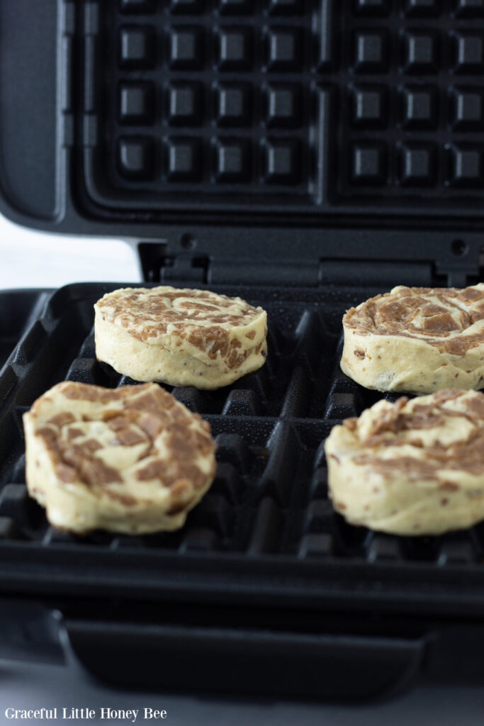 Store-bought cinnamon roll dough in the waffle iron before cooking.