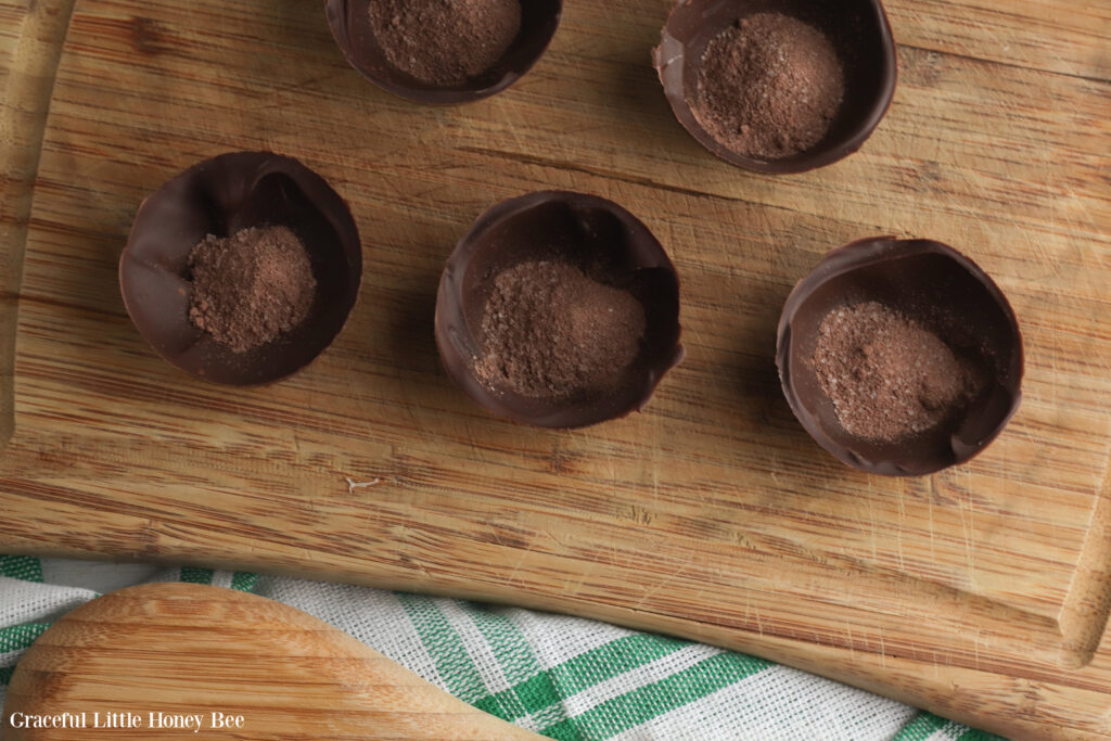 Half of the hardened chocolate filled with hot cocoa mix sitting on a wooden cutting board.