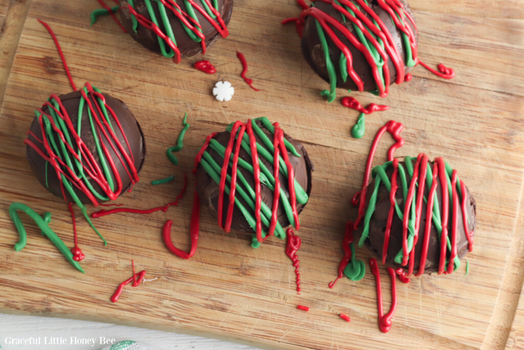 Finished hot chocolate bombs drizzled with red and green icing sitting on a wooden cutting board.