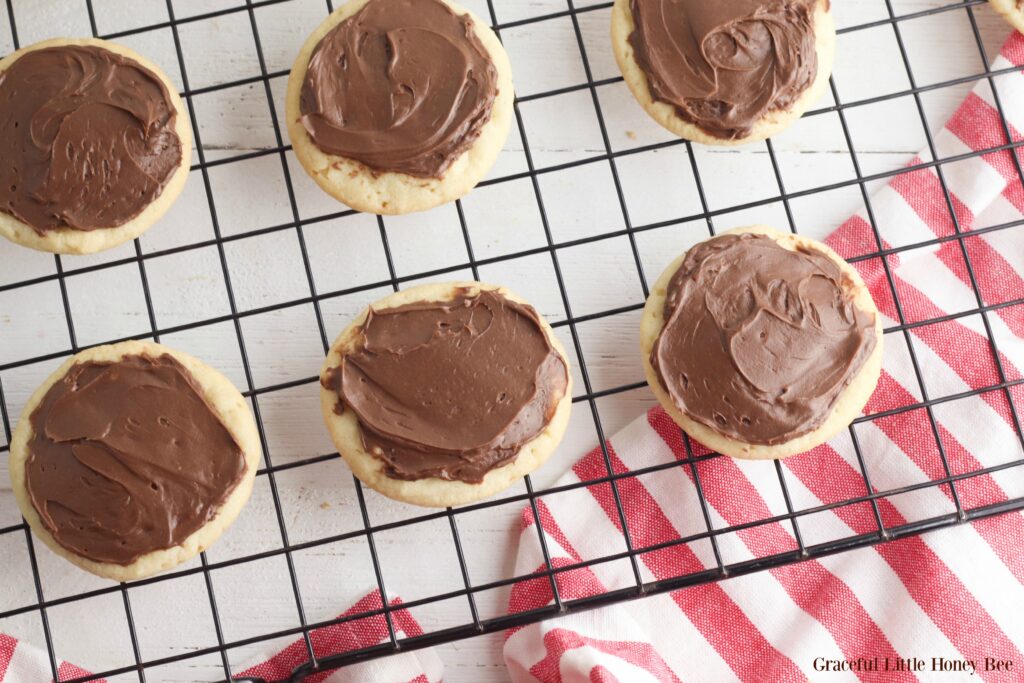 Sugar cookies with chocolate frosting sitting on a cooling rack.