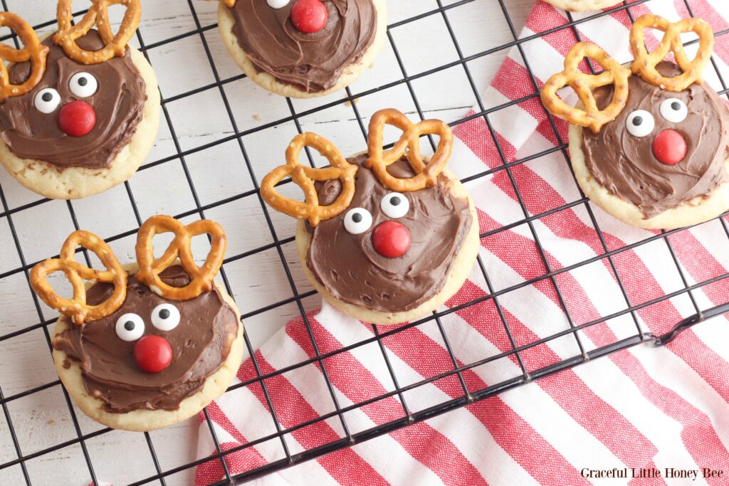 Finished reindeer cookies sitting on a black wire cooking rack with a red and white checked towel underneath.