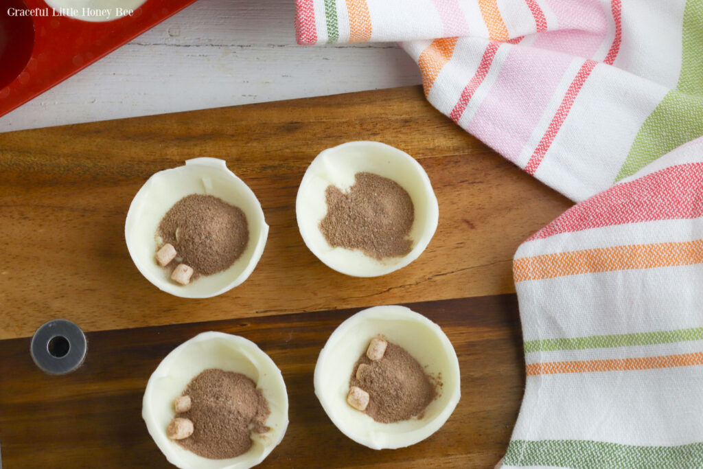 Four halfs of a hot chocolate bomb with instant hot chocolate mix inside sitting on a wooden cutting board.