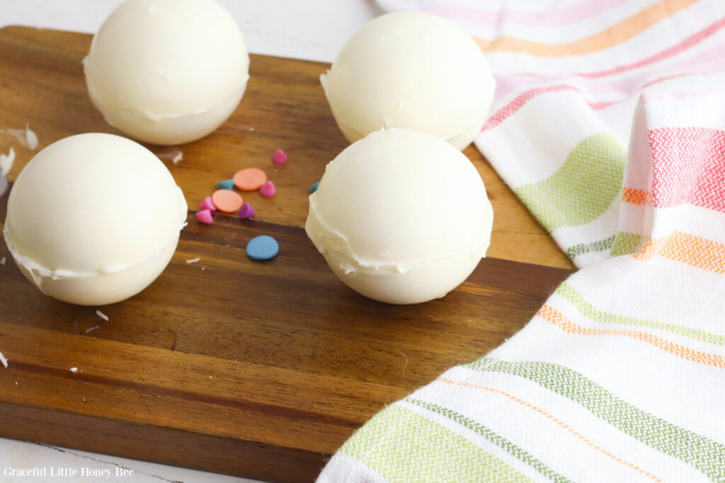 White hot chocolate bombs without toppings sitting on a wooden cutting board.