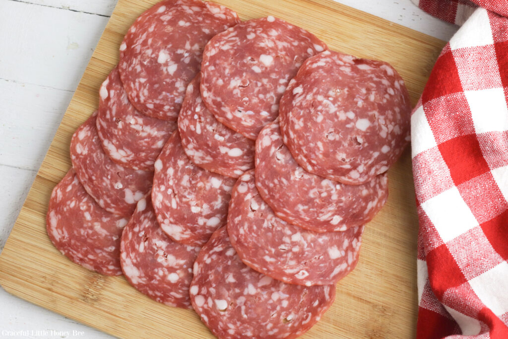 A layer of salami laid out on a wooden cutting board.