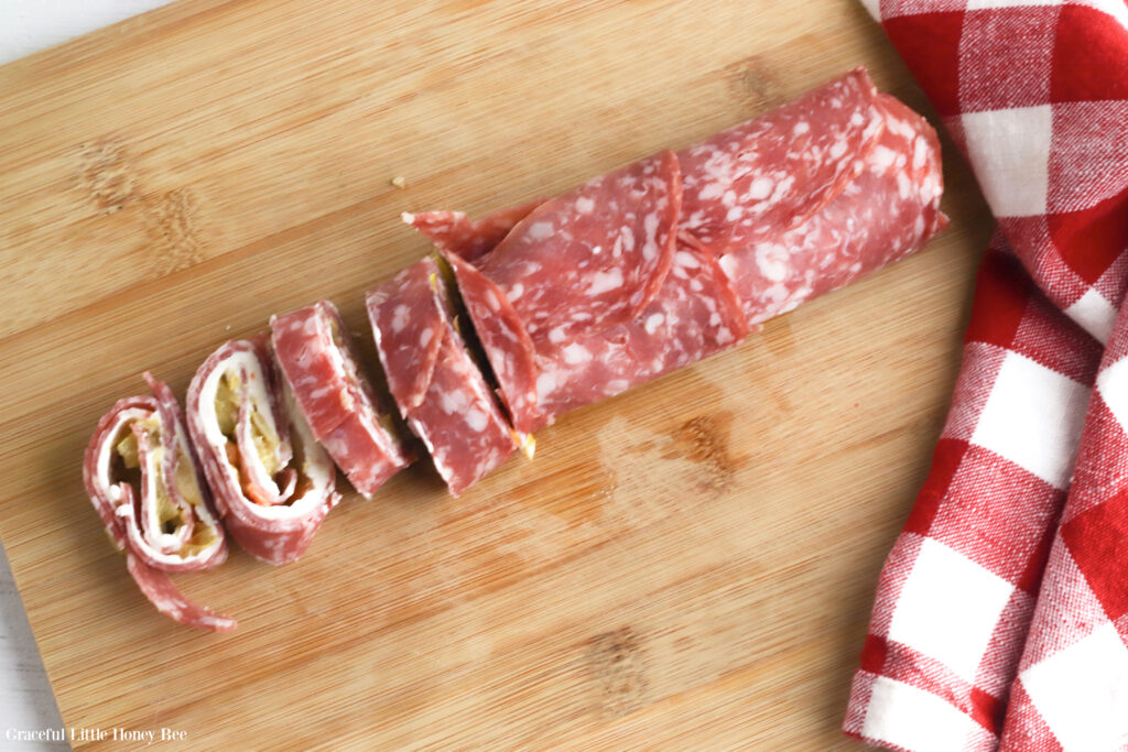 Lunchmeat, cheese and peppers rolled up into a log sitting on a wooden cutting board.