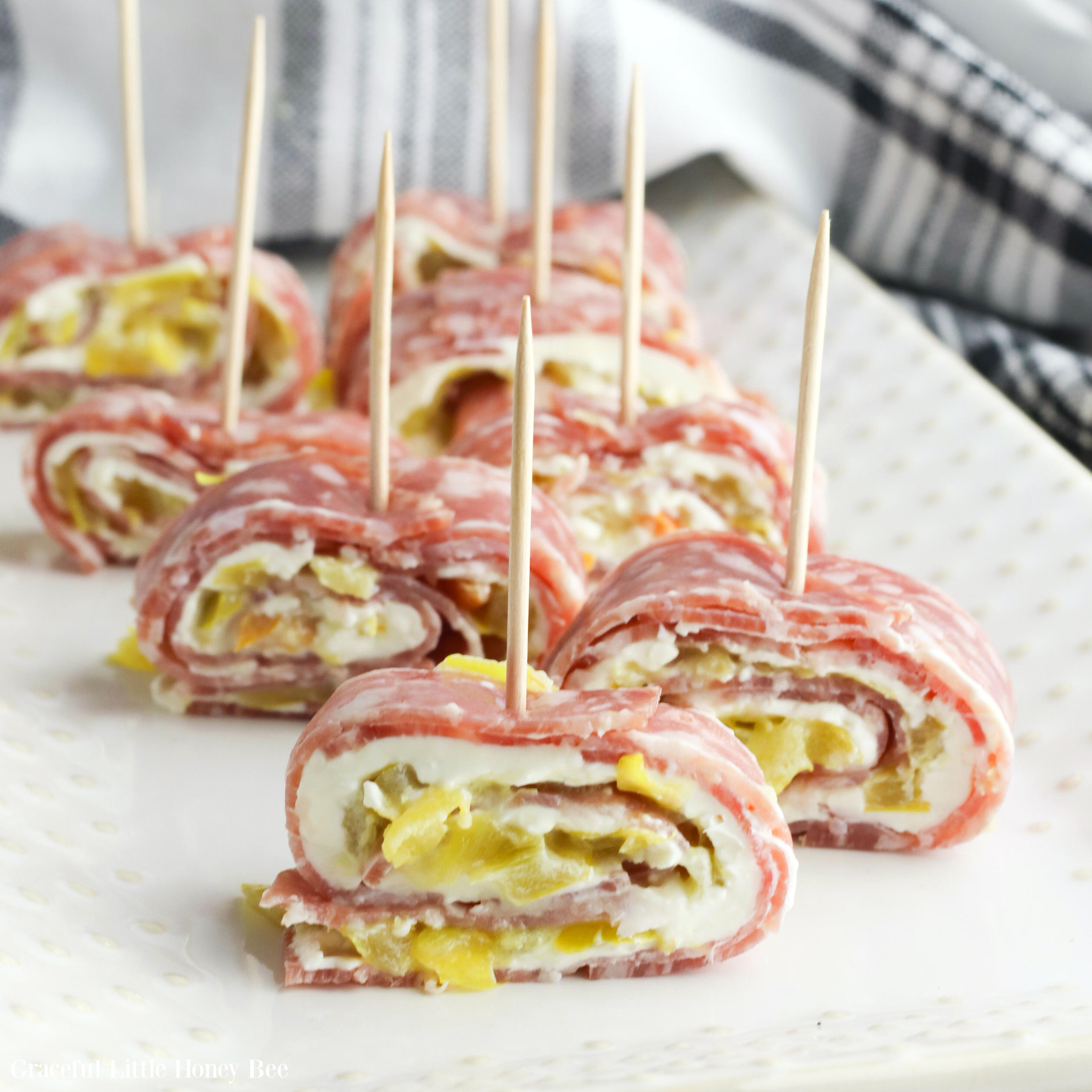 Salami Roll-Ups sitting on a white plate with a toothpick in each one.