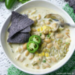 Chicken Enchilada Soup in a white bowl topped with blue corn tortilla chips and fresh slices of jalapenos.