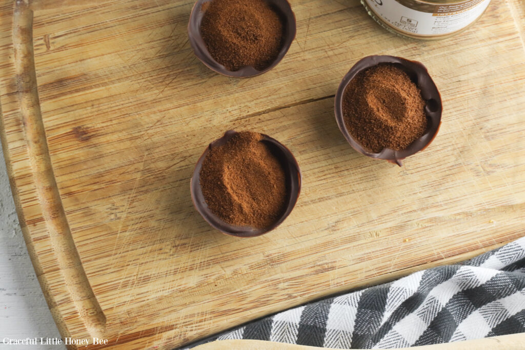 Three chocolate shell halves filled with espresso powder sitting on a wooden cutting board.