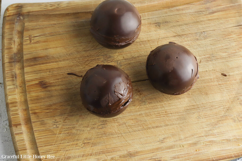 Three Hot Chocolate Bombs sitting on a wooden cutting board.