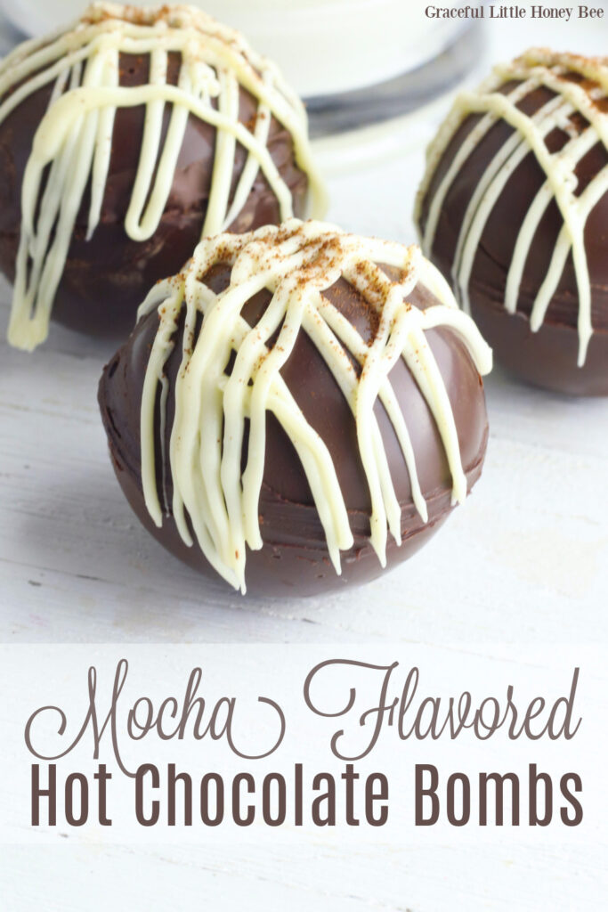 Mocha Hot Chocolate Bombs drizzled with white chocolate candy coating, sitting on a white countertop.