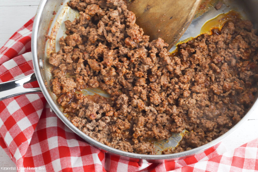 Cooked ground beef seasoned with taco seasoning in a metal pan.