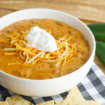 Queso Taco Dip in a white bowl topped with shredded cheese and sour cream.