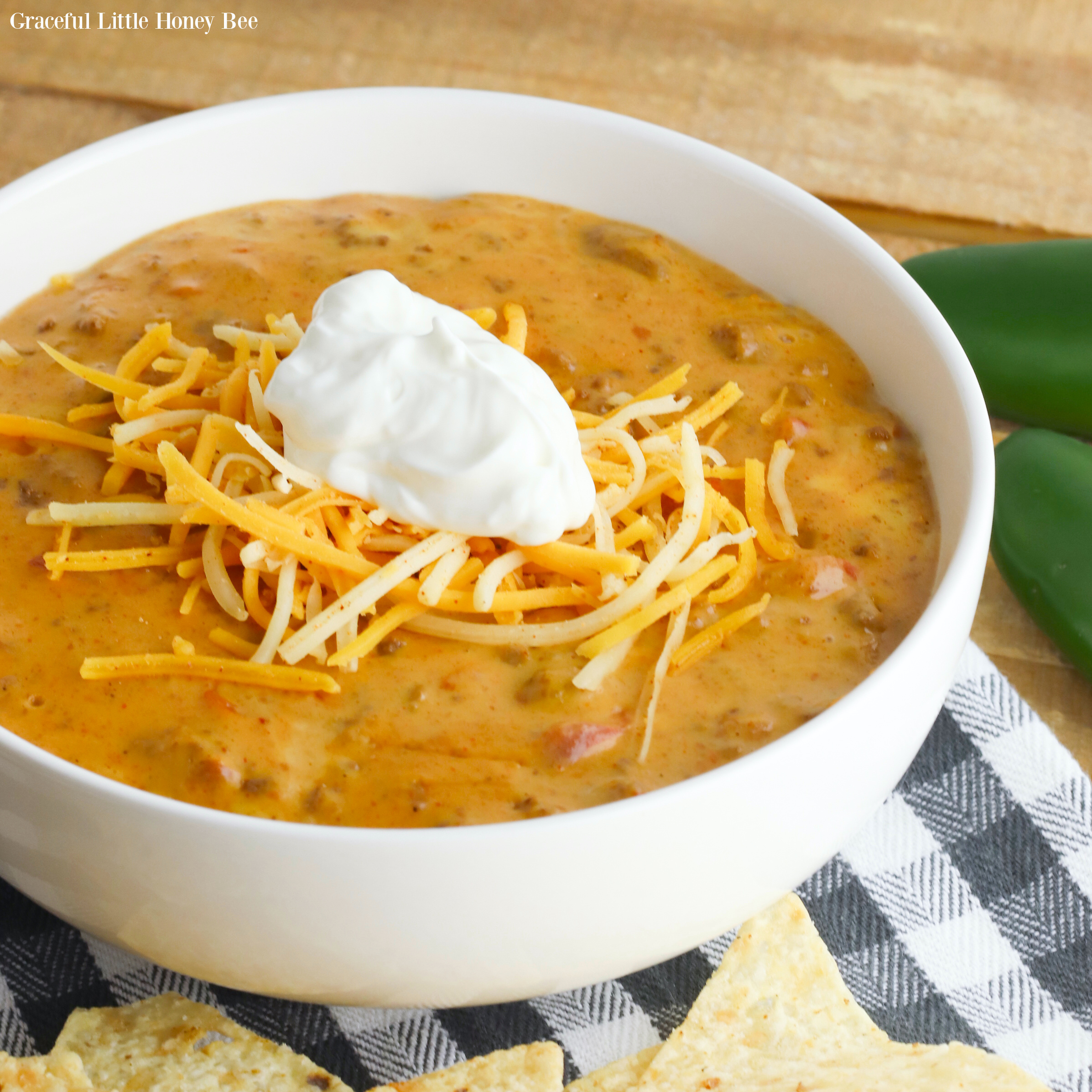 Queso Taco Dip in a white bowl topped with shredded cheese and sour cream.