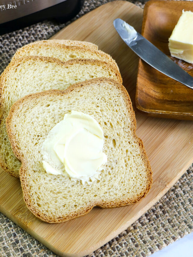 Three slices of white bread with a slab of butter sitting on a cutting board.