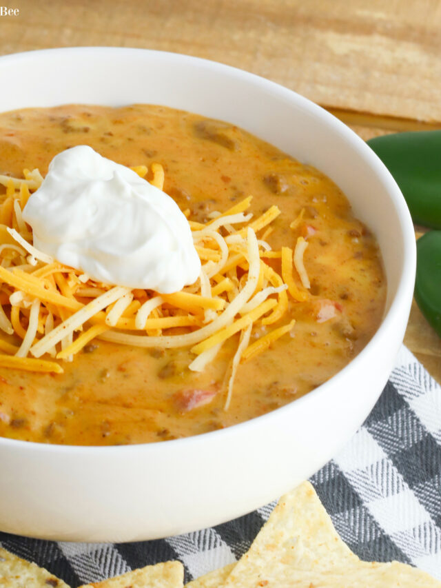 Queso Taco Dip in a white bowl topped with shredded cheese and sour cream.