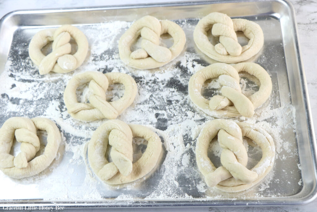 Pretzel dough made into pretzel shapes, sitting on a metal baking sheet.