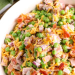 A large white serving bowl filled with Ham and Green Pea Salad.