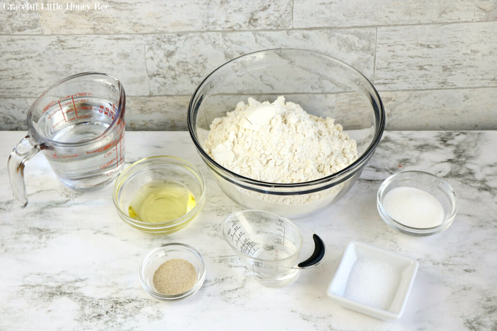 All ingredients for pizza dough sitting separately on a marble counter.