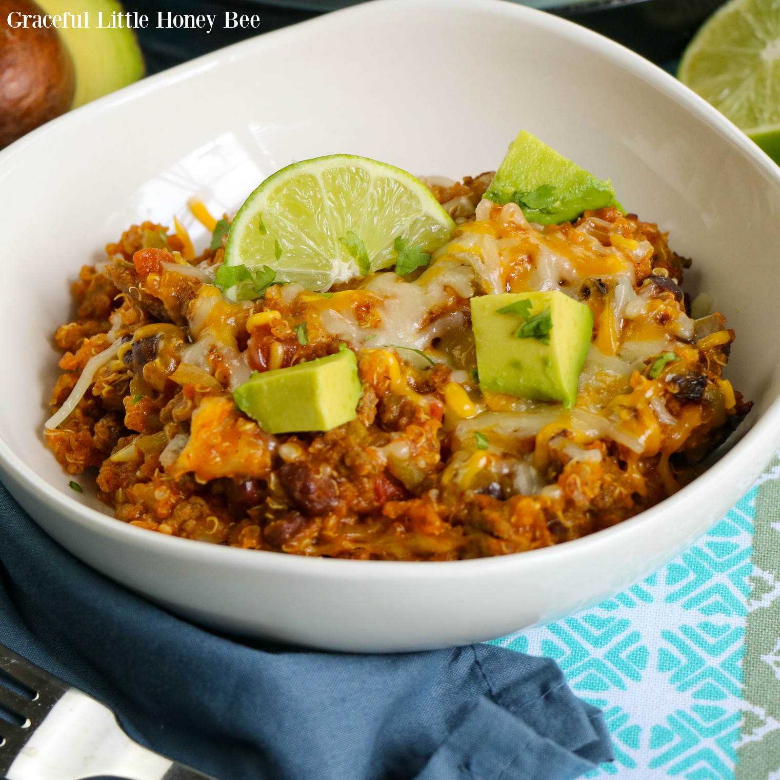 Quinoa Enchilada Casserole in a white bowl topped with cheese and garnished with lime.