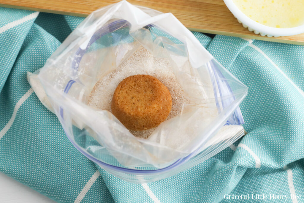 Muffin upside down in a bag full of cinnamon sugar mixture sitting on a teal tea towel.