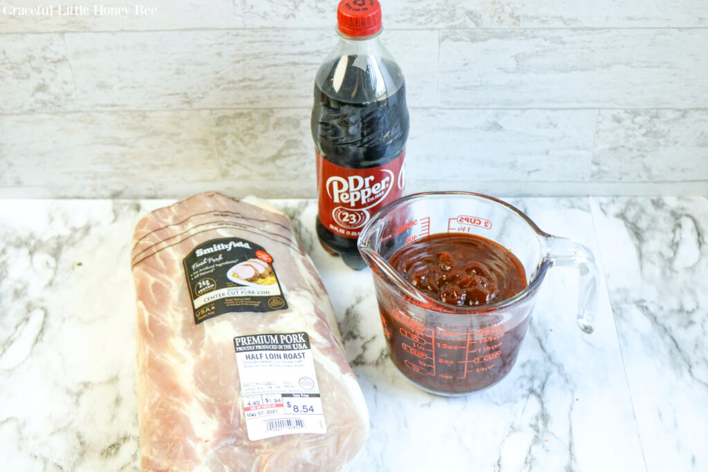 Boneless pork tenderloin, BBQ sauce and a bottle of Dr. Pepper sitting on a marble countertop.