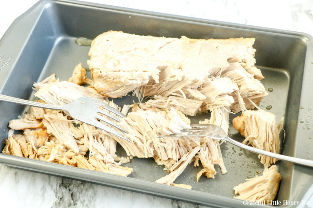 Cooked tenderloin in a pan in the process of being shredded with two forks.