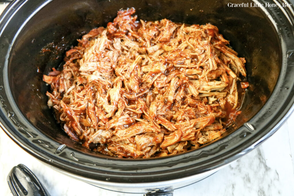 Shredded pork covered in BBQ sauce in a black slow cooker.