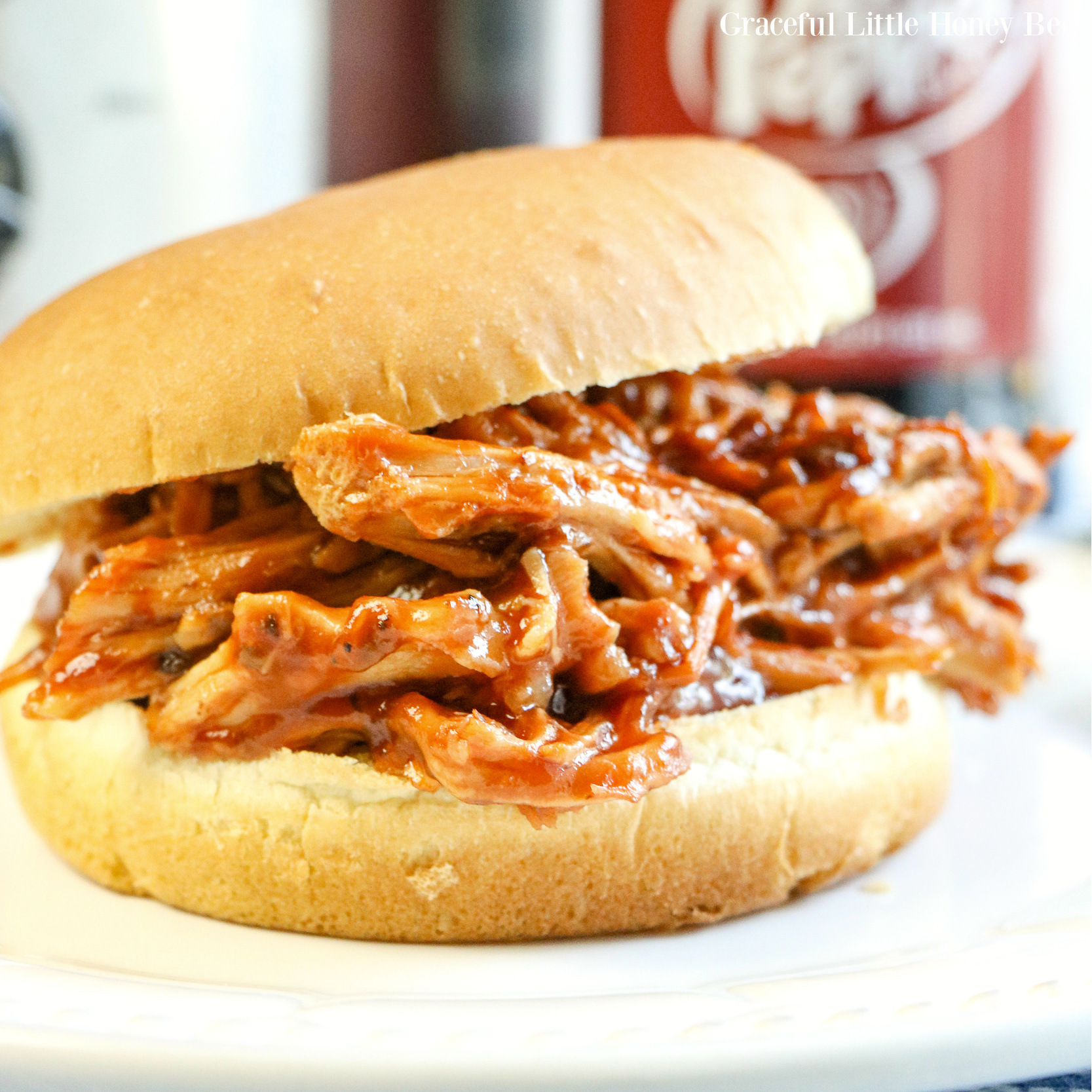 Pulled Pork Sandwhich sitting a on white plate with a bottle of Dr. Pepper in the background.