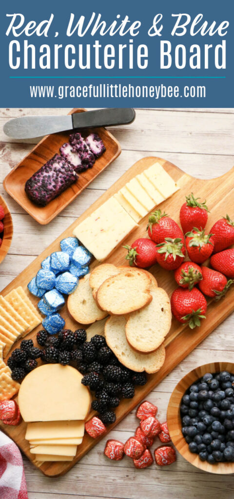 An assortment of red, white and blue finger food arranged neatly on a cutting board including strawberries, blueberries, crackers, cheese and chocolate.