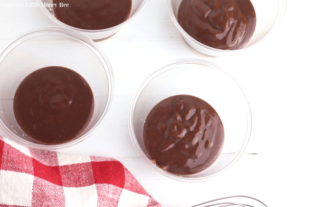 Chocolate pudding layered on top of graham cracker crumbs in clear plastic cups.