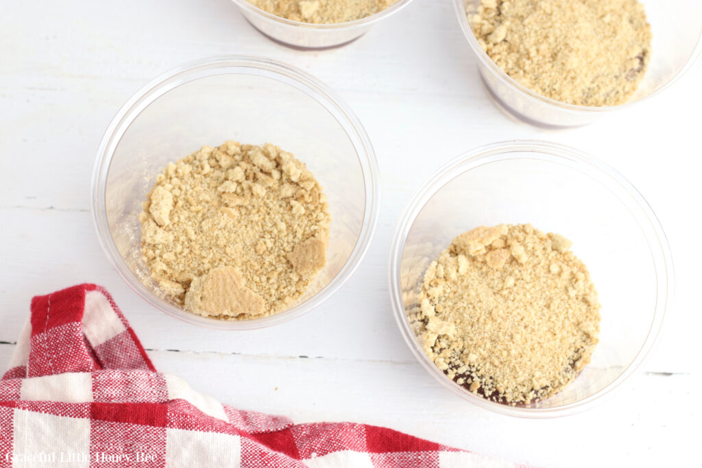 A second layer of graham cracker crumbs on top of the chocolate pudding in clear plastic cups.