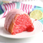 Slice of Cherry Limeade Bundt Cake garnished with a cherry on a small round white plate.