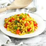 Fiesta Corn served on a round white plate with a wooden spoon in the background.