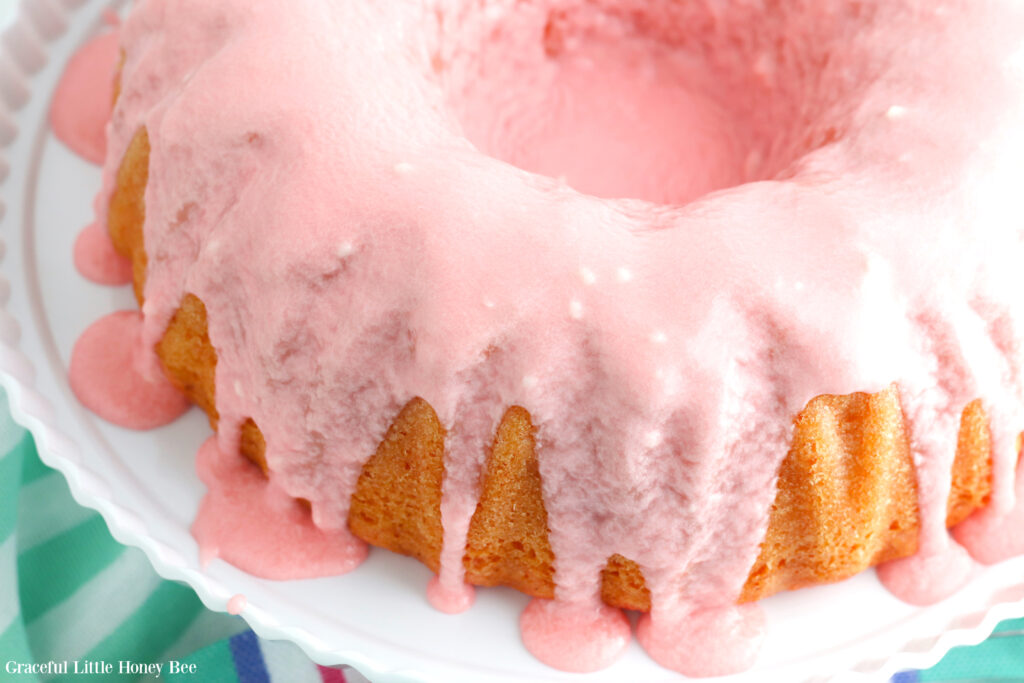 Finished bundt cake drizzled with pink glaze on a round white cake platter.