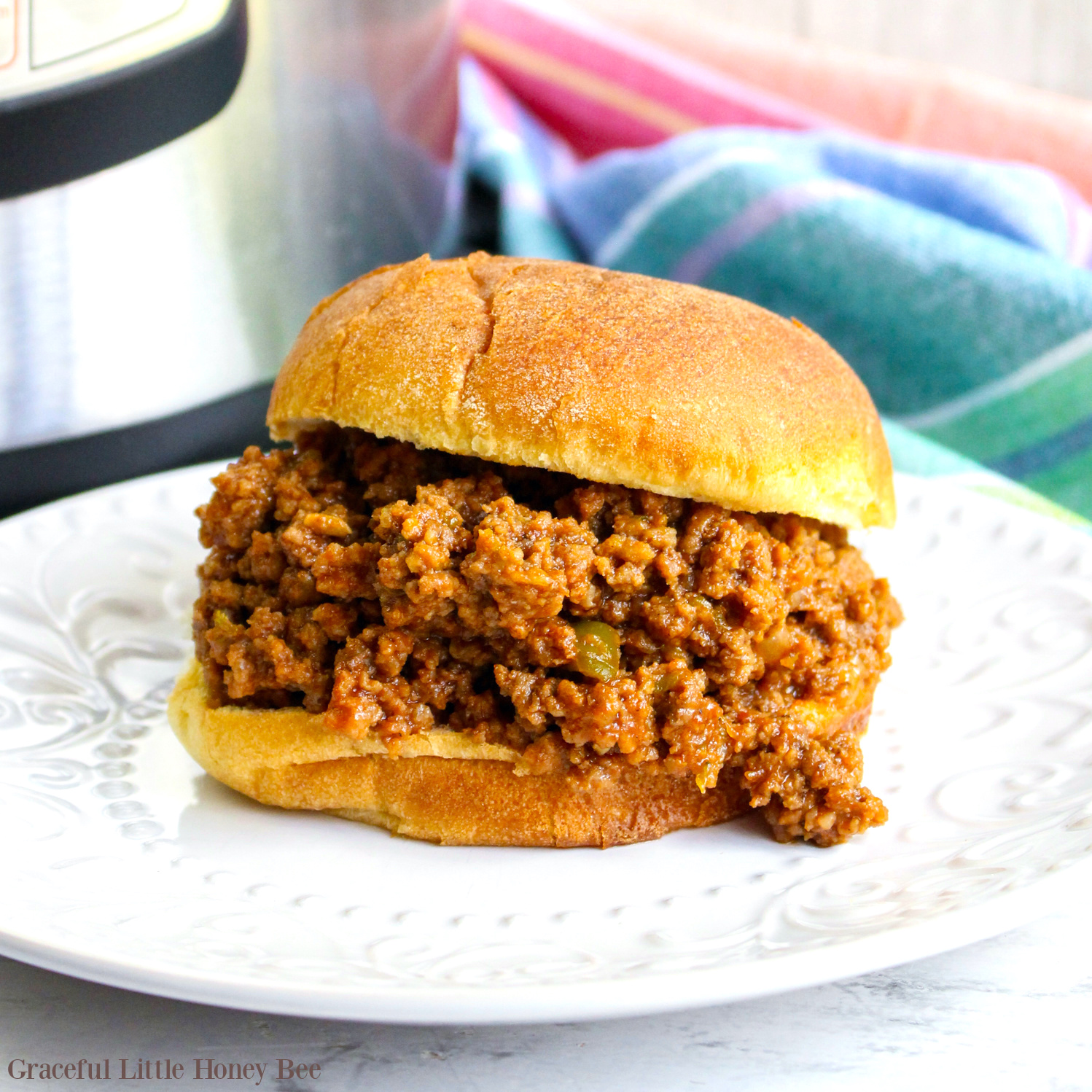 Sloppy Joes on hamburger bun sitting on a round white plate.