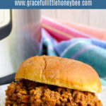 Sloppy Joes served on hamburger bun on a white plate with Instant Pot in the background.