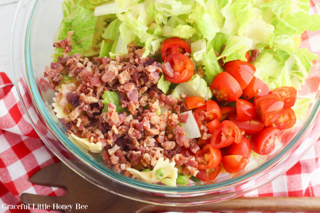 Chopped lettuce, bacon and tomatoes in a large glass mixing bowl.