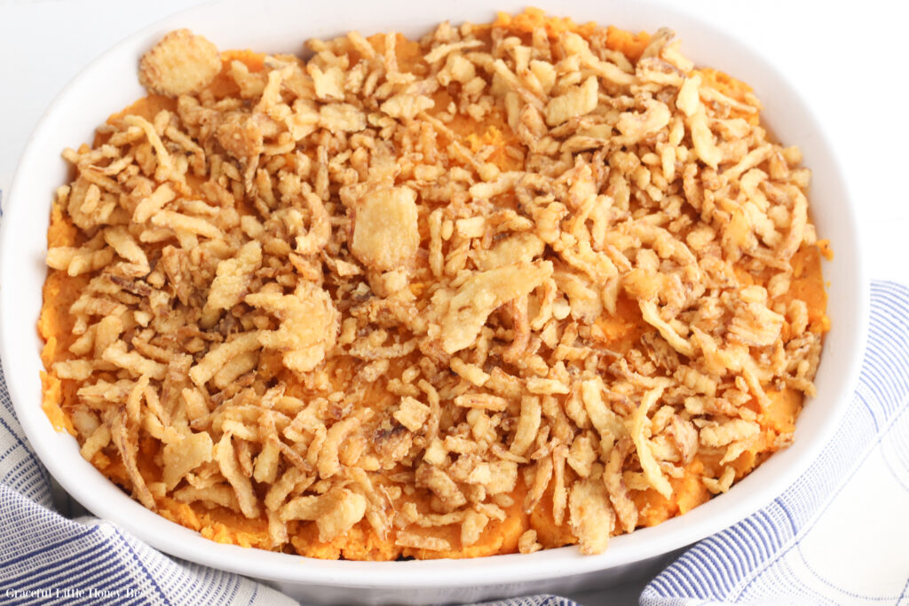 French fried oniions sprinkled on top of mashed sweet potatoes in white baking dish.