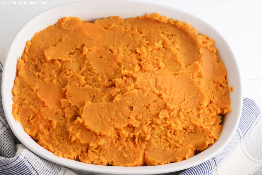 Mashed sweet potato on top of vegetable mixture in white baking dish.