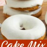 A stack of iced donuts sitting on a wooden cutting board.