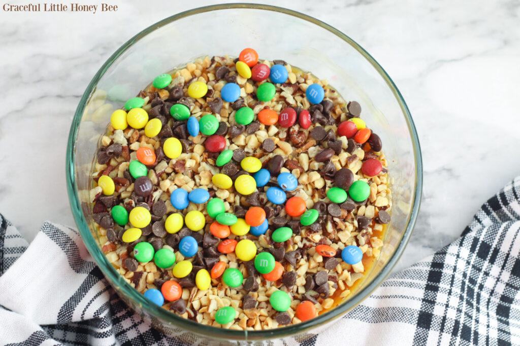 Caramel Apple dip with Peanuts and Chocolate Candy in a clear glass bowl.